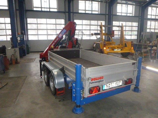 Tandem-axle flatbed trailer fitted with an HMF knuckleboom loader crane and four hydraulic outriggers—ideal for lifting and loading materials on job sites and service operations.